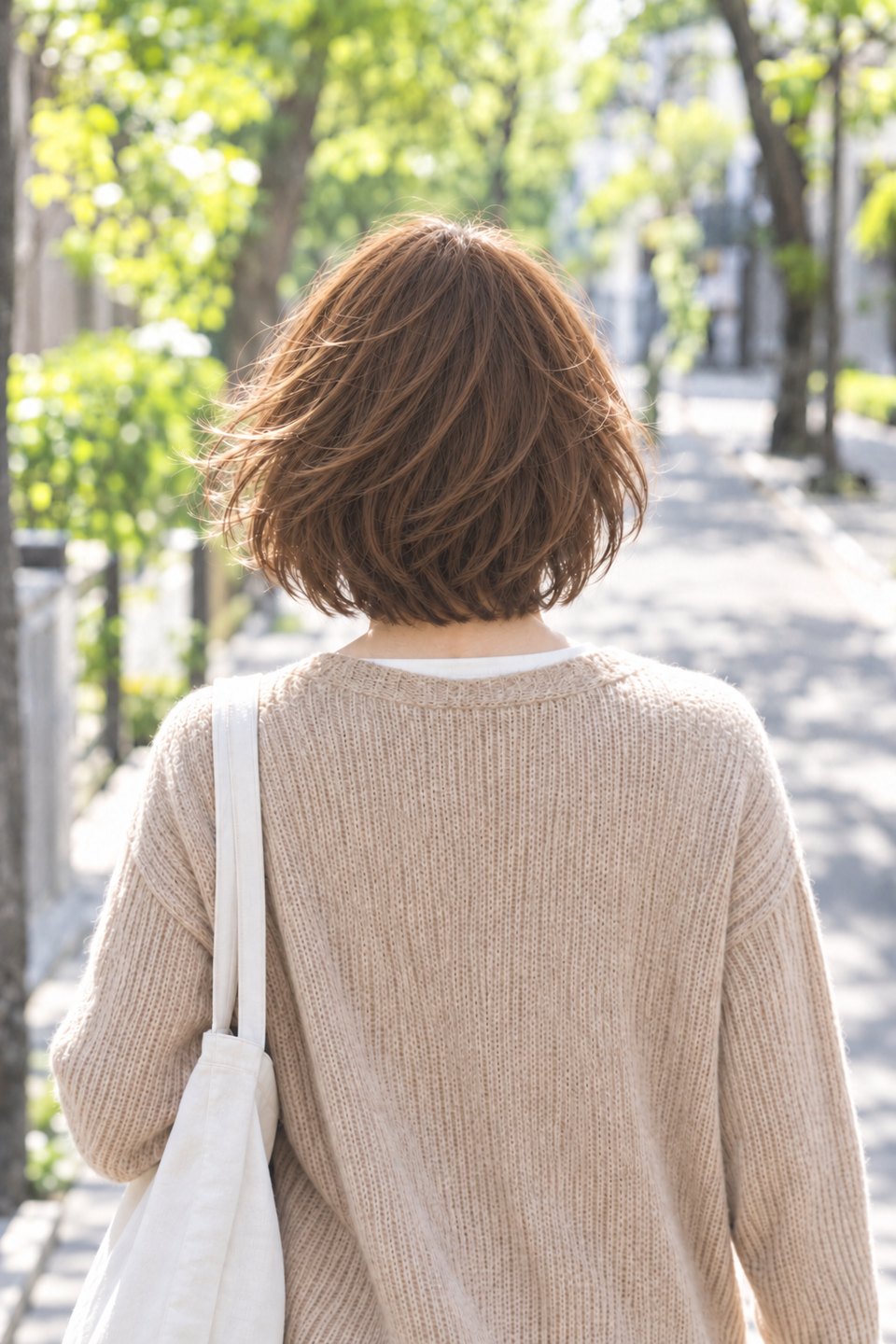並木道を歩く女性の後ろ姿。風に髪がなびく